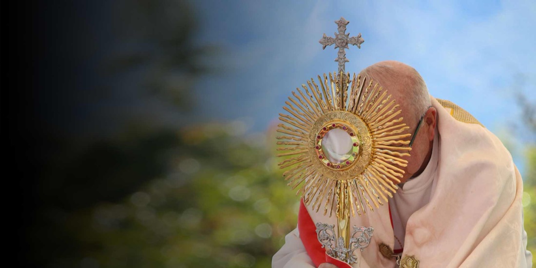 Un prêtre incline la tête devant l'ostensoir, lors d'une adoration en plein air.