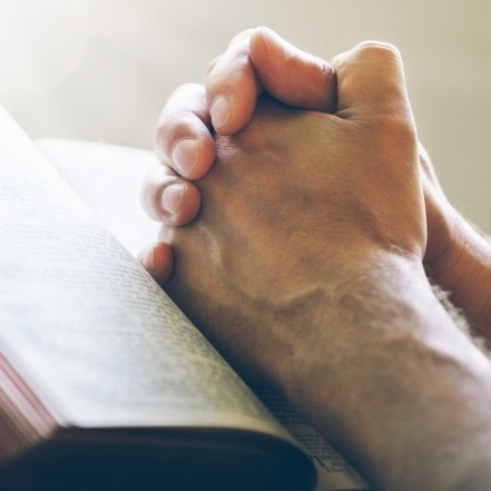 Deux mains jointes posées sur une bible ouverte.