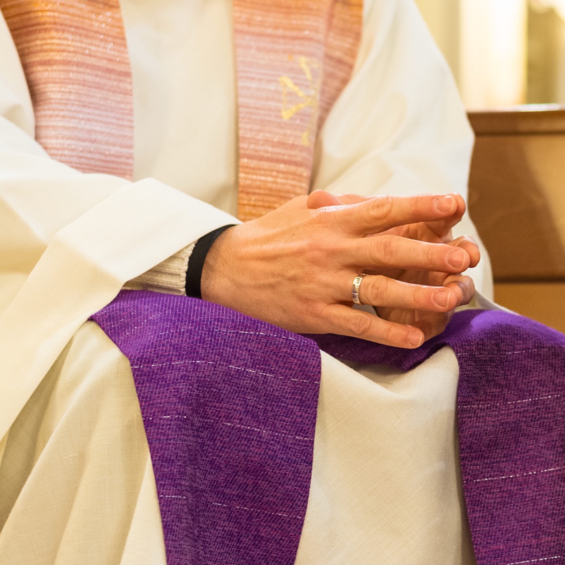 Les mains jointes d’un prêtre revêtu de l’aube et de l’étole violette.