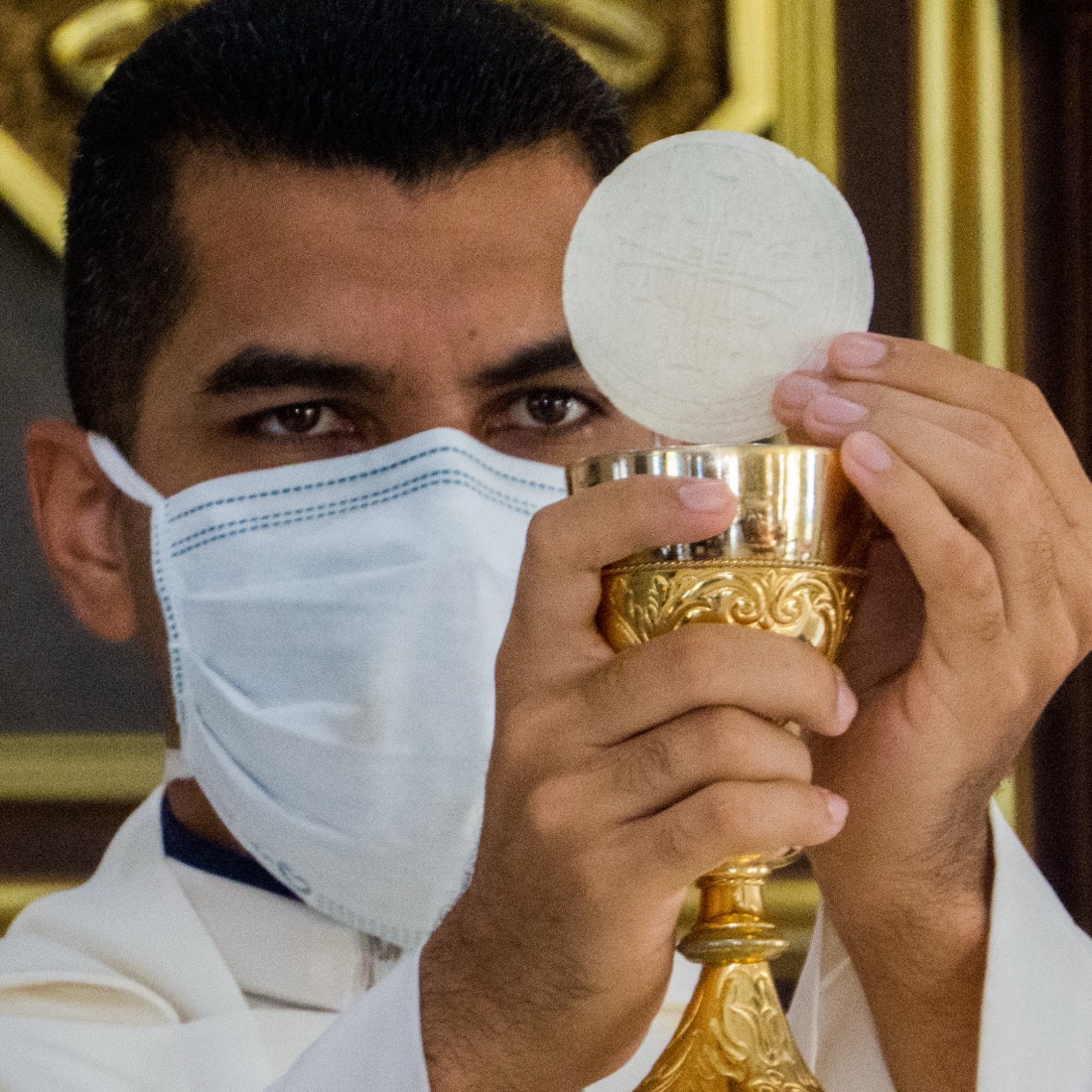 Un prêtre célèbre la messe, les mains levées au-dessus de l’autel.
